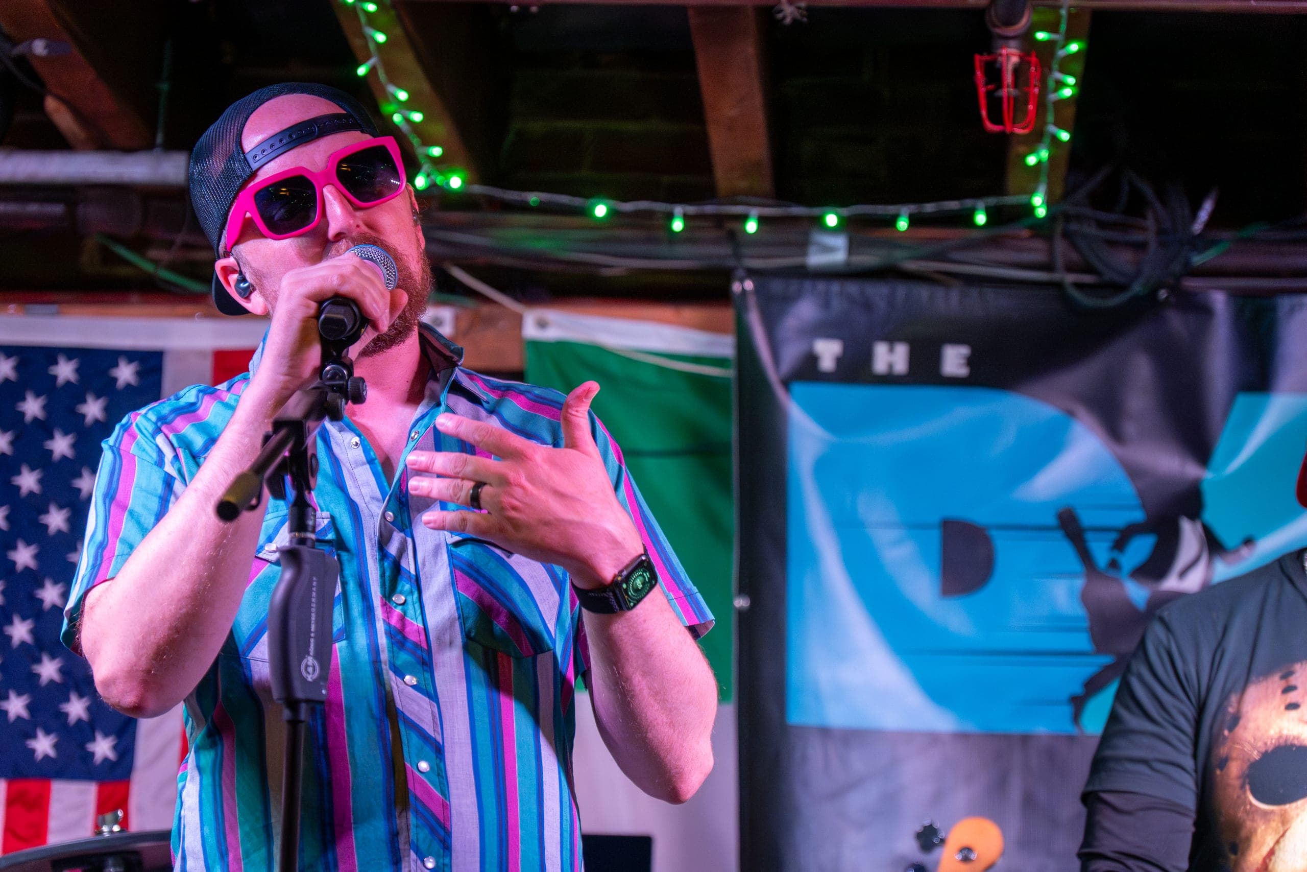 Singer in pink sunglasses and a striped shirt commanding the mic at a pub gig